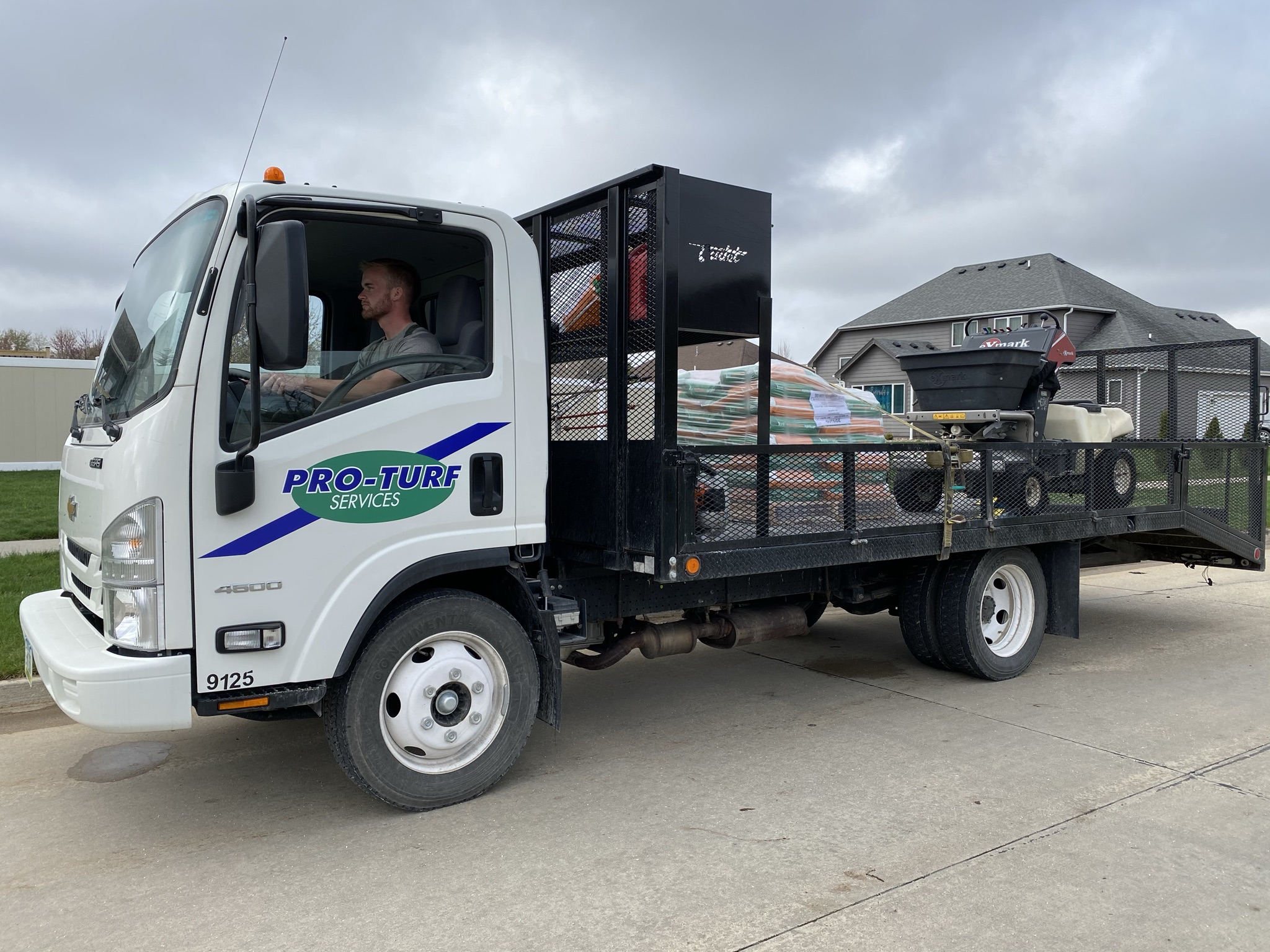 A PRO-TURF Services lawn care professional drives a yard maintenance truck with lawn care tools in the trailer.